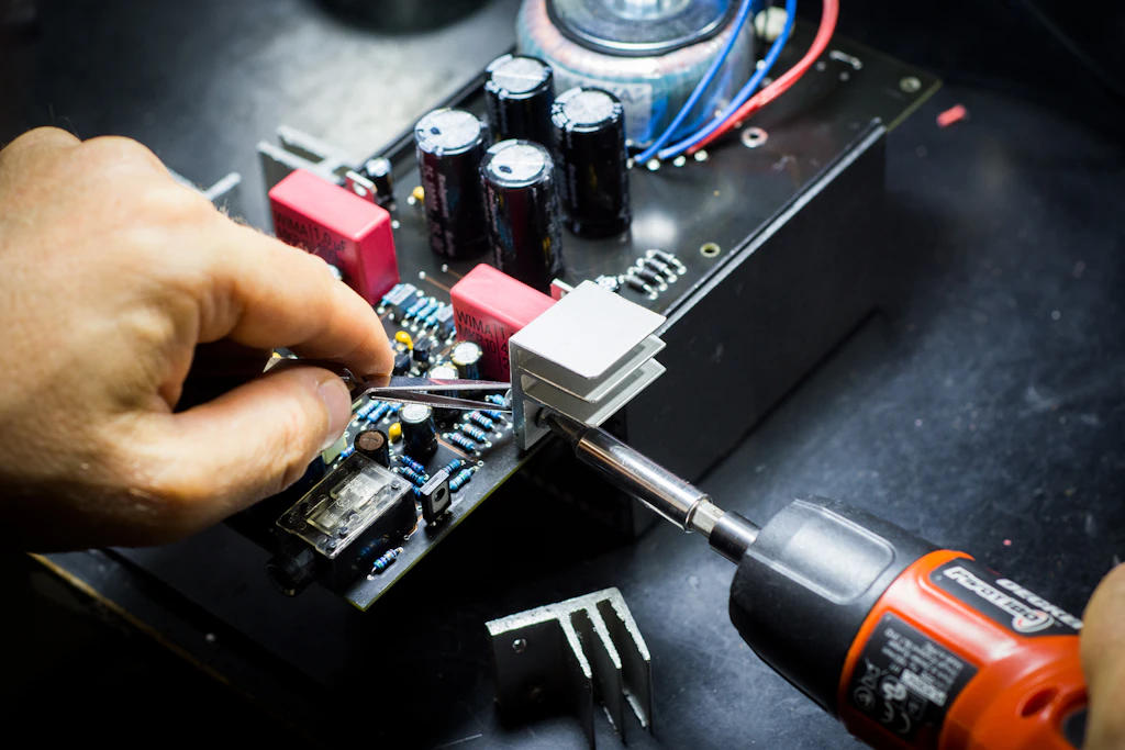 Hands performing detailed electronics work on a circuit board at a workbench
